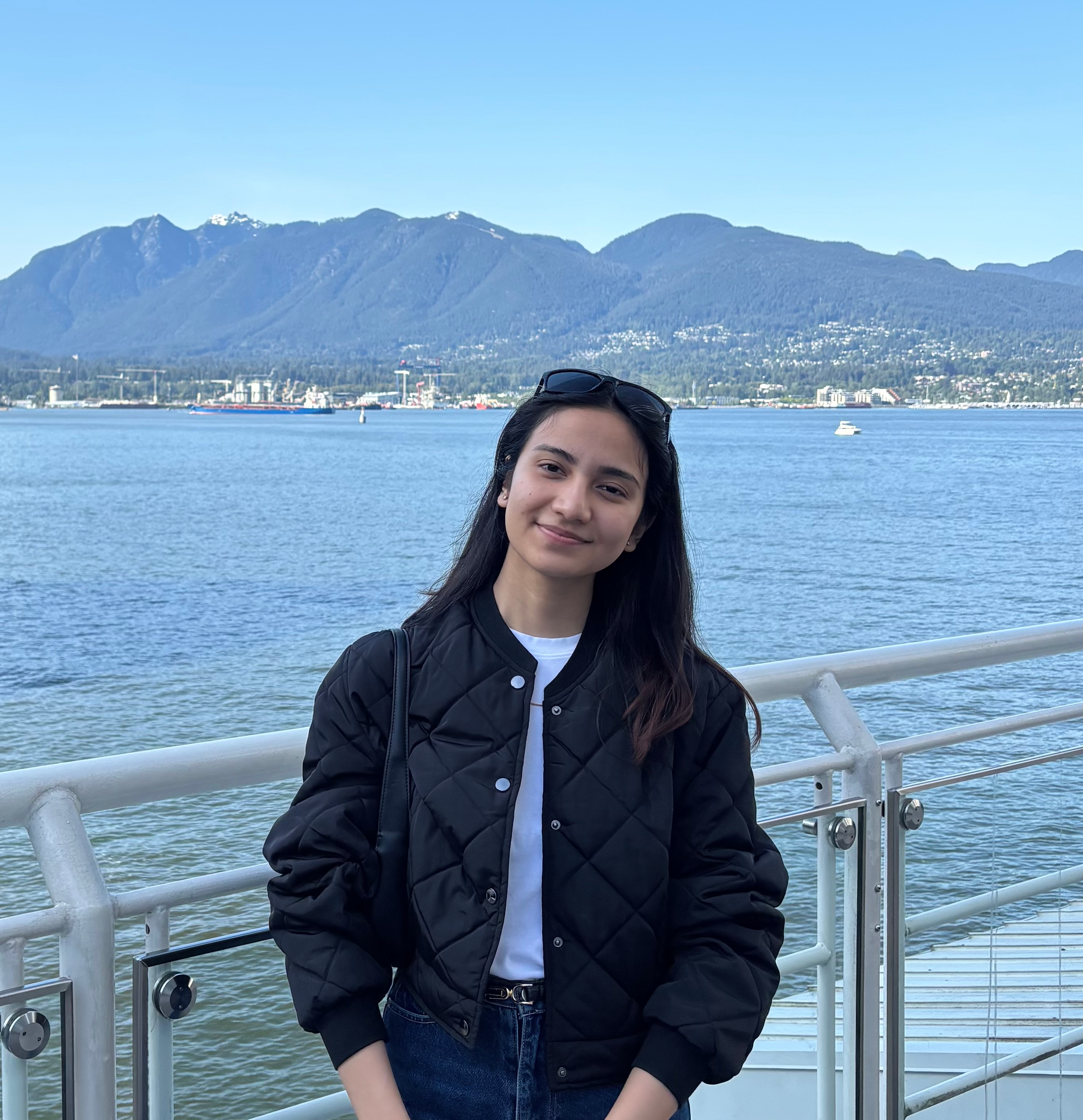 Usha smiling by a waterfront railing, with the sea and mountains behind her