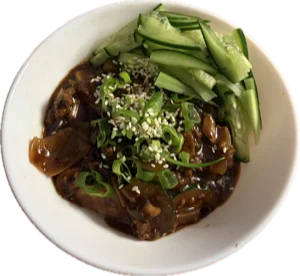 A bowl of black bean sauce noodles topped with cucumber, spring onion and sesame